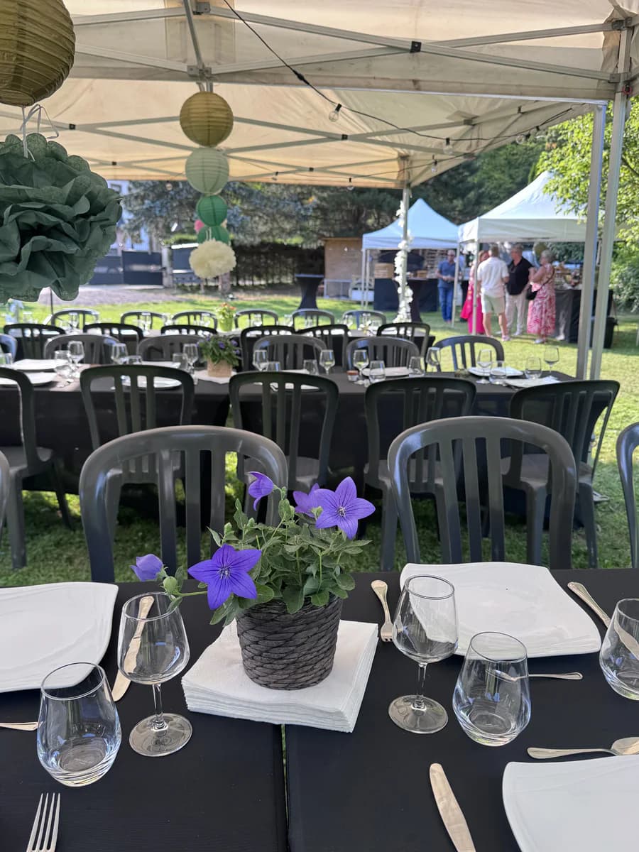 Tables nappées, vaisselle et chaises installées sous un barnum dans un jardin