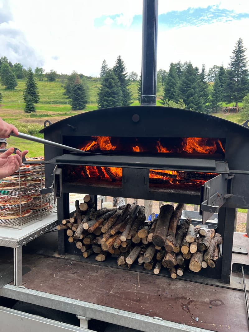 Four à bois mobile ouvert avec les bûches rangées sous la chambre de cuisson