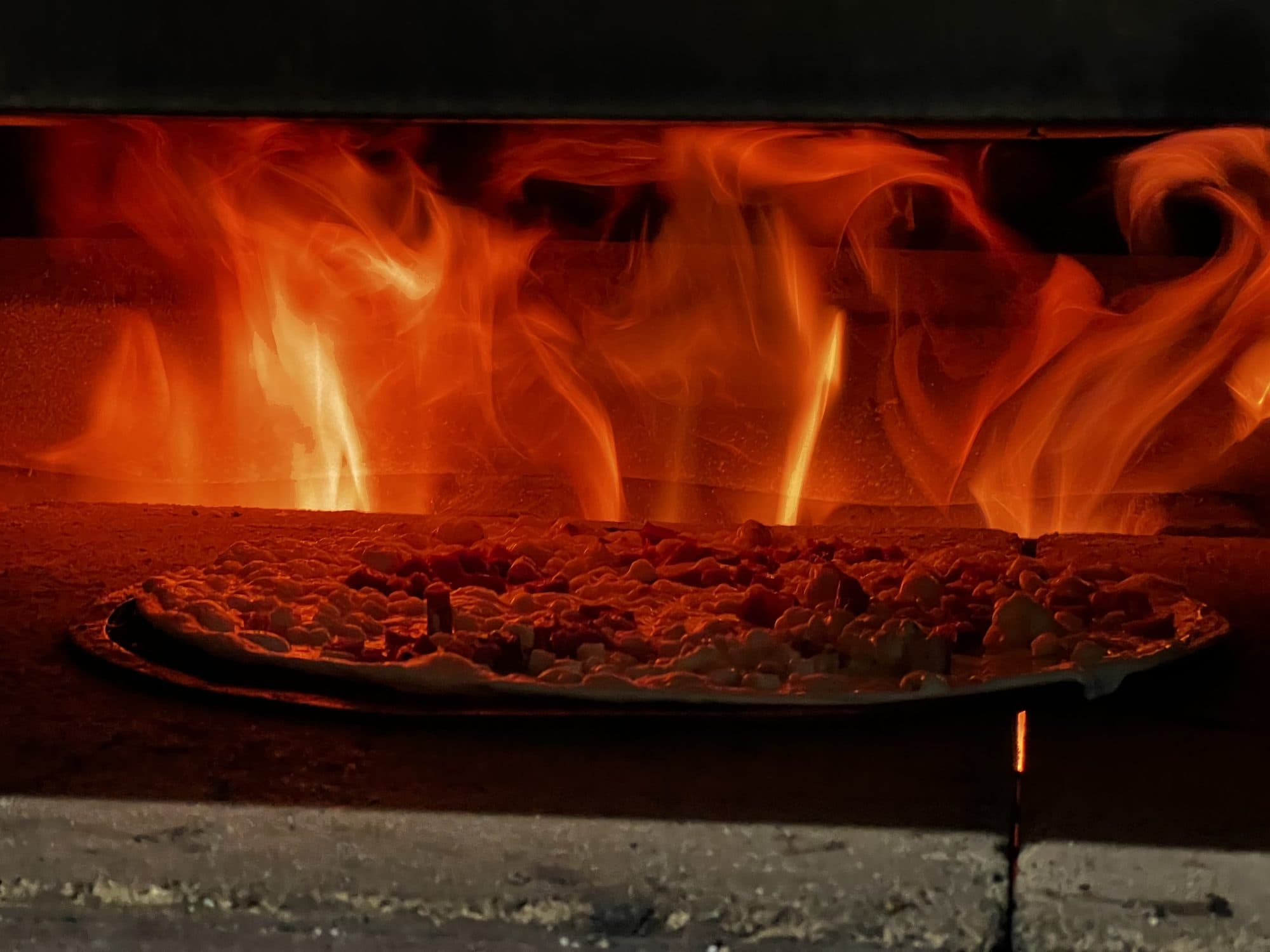 Tarte flambée en cuisson devant les flammes du four à bois