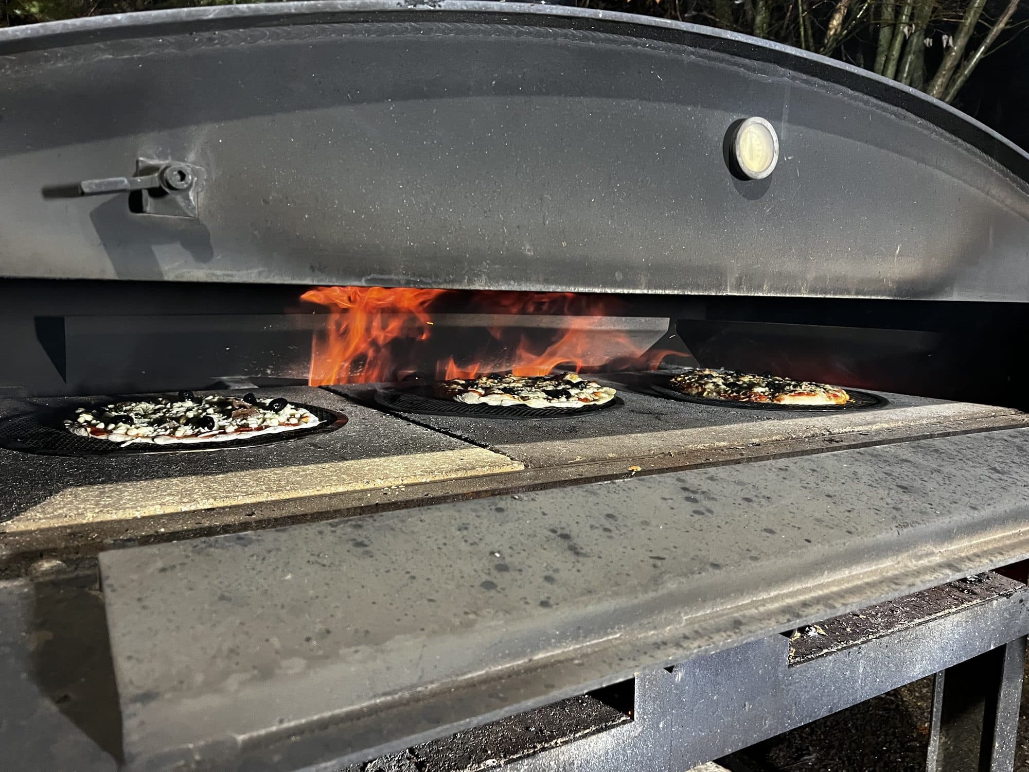Plusieurs tartes flambées cuisent côte à côte dans le four à bois
